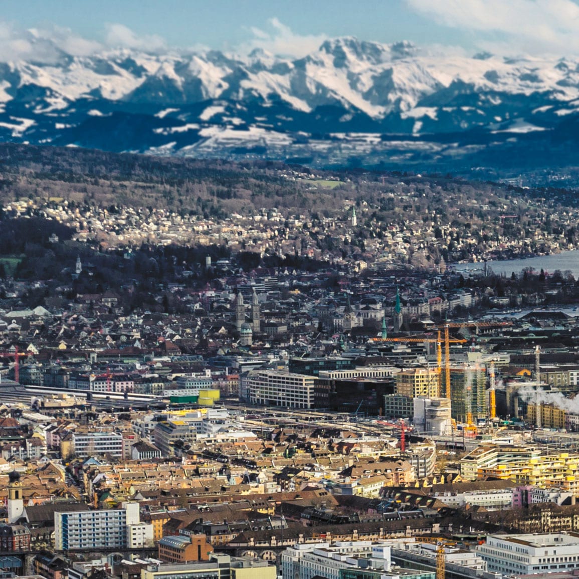 Luftaufnahme auf Zürich mit seinem See, mit schneebedeckten Bergen im Hintergrund.