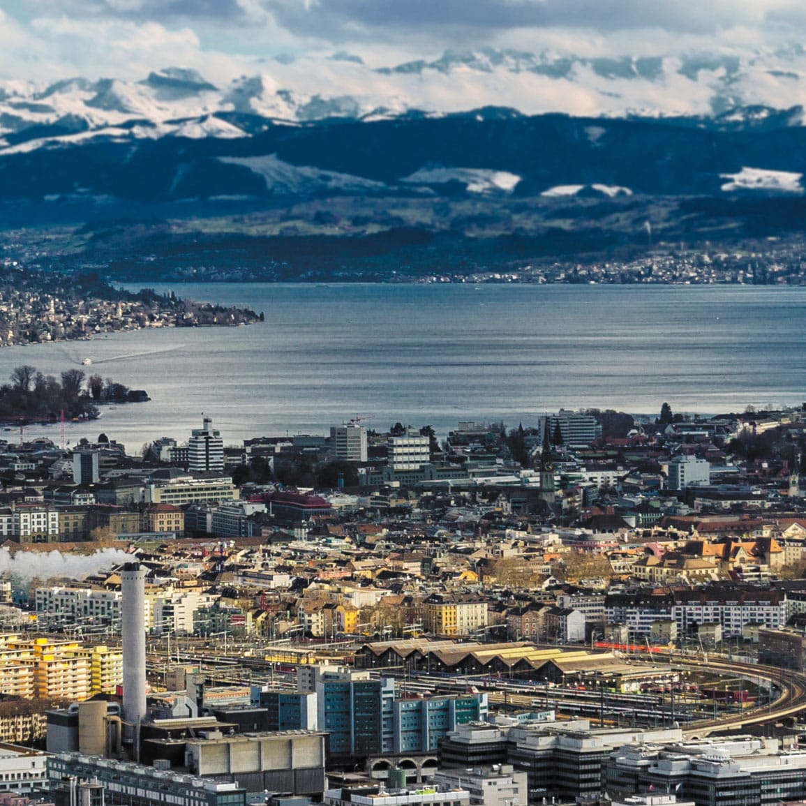 Luftaufnahme auf Zürich mit seinem See, mit schneebedeckten Bergen im Hintergrund.