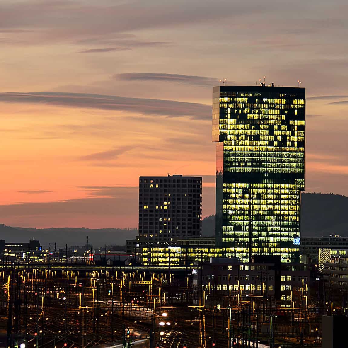 Die Skyline von Zürich bei Sonnenuntergang mit Hügeln im Hintergrund.