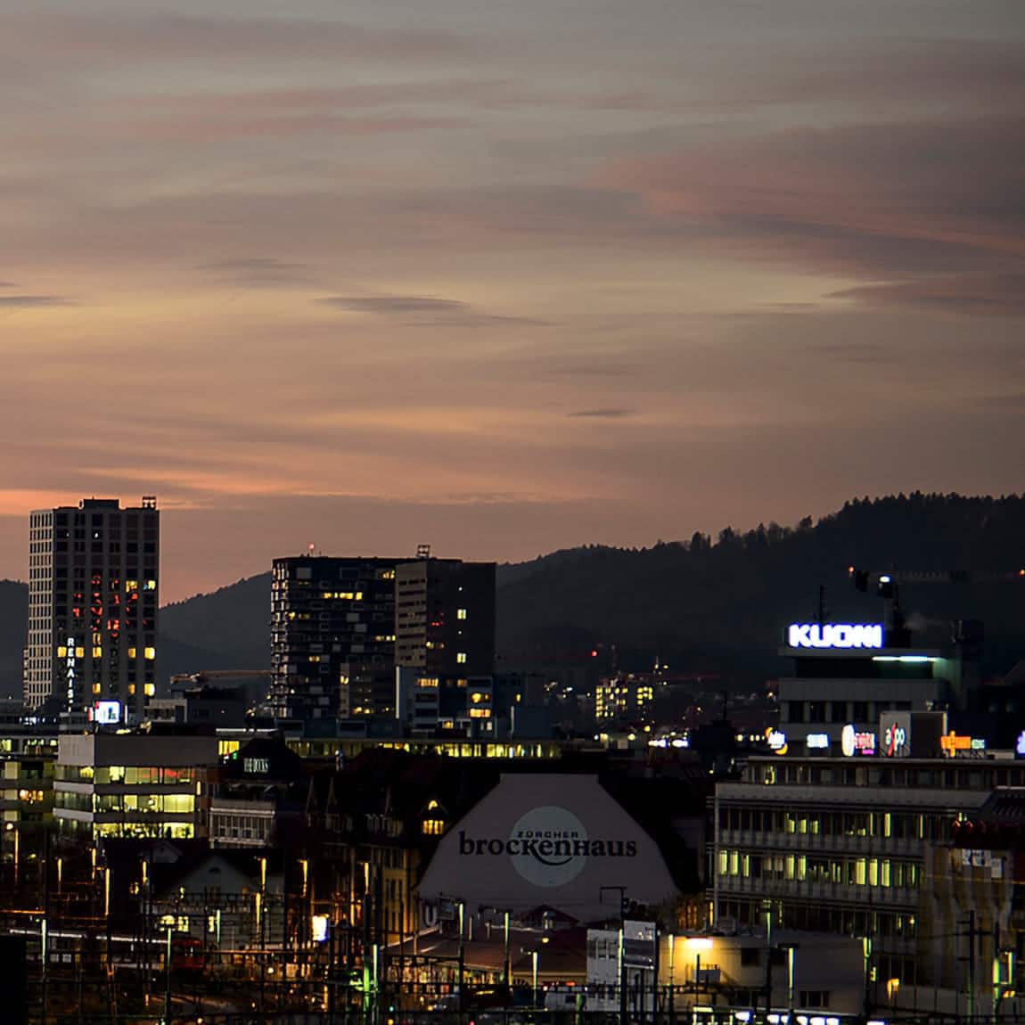 Die Skyline von Zürich bei Sonnenuntergang mit Hügeln im Hintergrund.